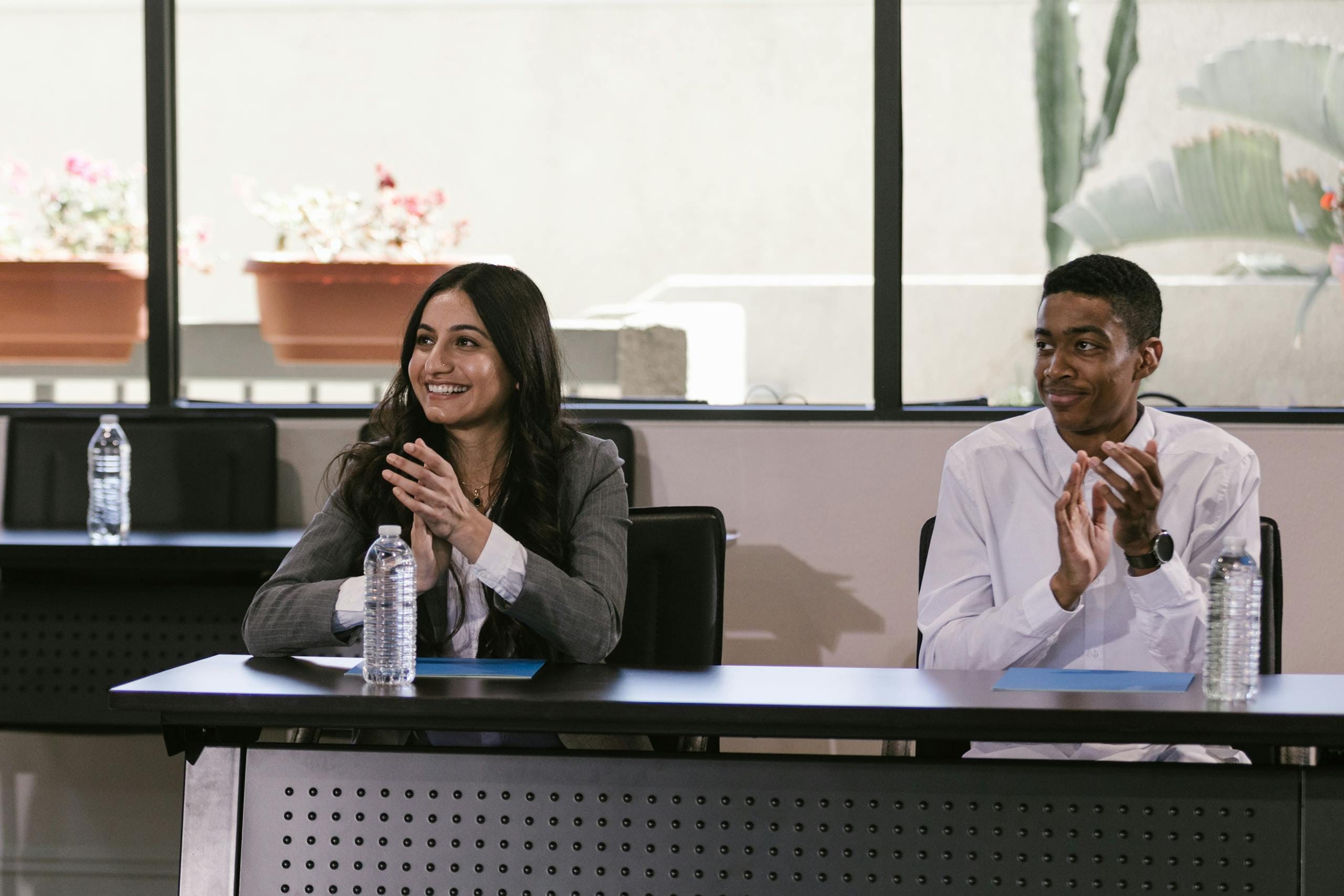 Smiling coworkers clapping at a table in a professional setting indoors.